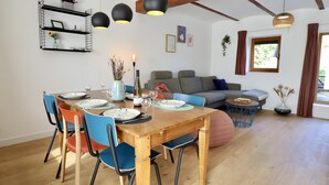Uma sala de jantar com uma mesa de madeira posta para quatro pessoas, rodeada por cadeiras coloridas.