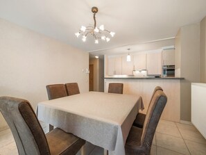 A dining area with a table and chairs, a kitchen in the background, and a chandelier. - Beautiful 2-Bedroom Apartment in City Center (Blankenberge)