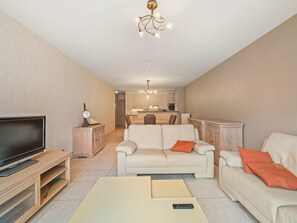 A modern living room with a flat-screen TV, a sofa, a coffee table, and a dining area in the background. - Beautiful 2-Bedroom Apartment in City Center (Blankenberge)