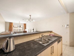 A modern kitchen with a large island, stainless steel sink, and a kettle. - Beautiful 2-Bedroom Apartment in City Center (Blankenberge)