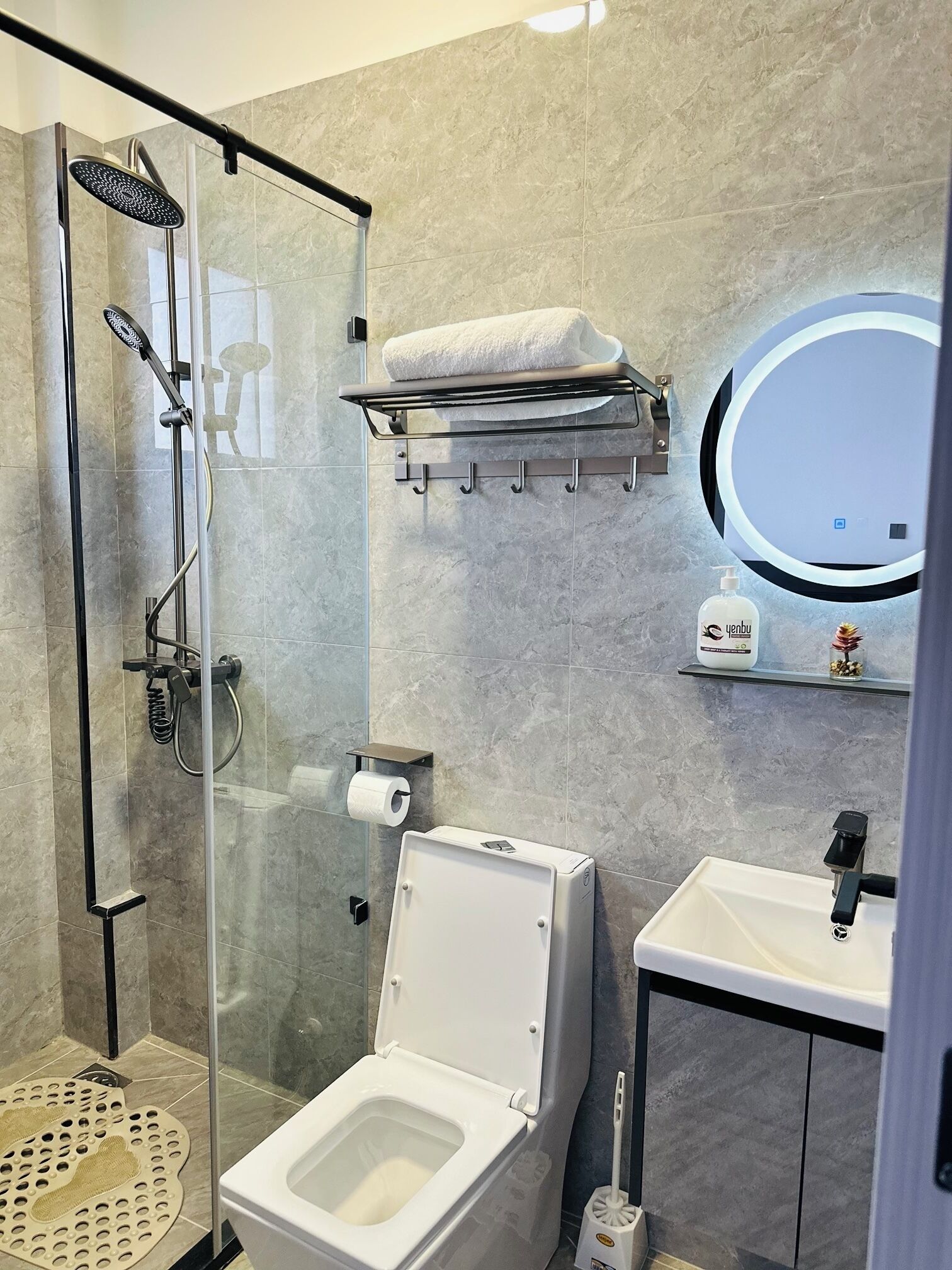 A modern bathroom with a glass-enclosed shower, a toilet, a sink, and a small shelf with toiletries.