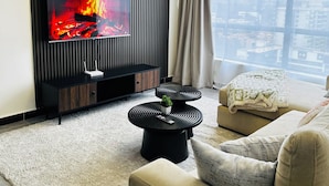 A modern living room with a flat-screen TV, a black entertainment unit, two black round tables, a beige sofa, and a large window with curtains. - 14th Floor 2B with Pool, Gym & King Bed in Lavington (Nairobi)