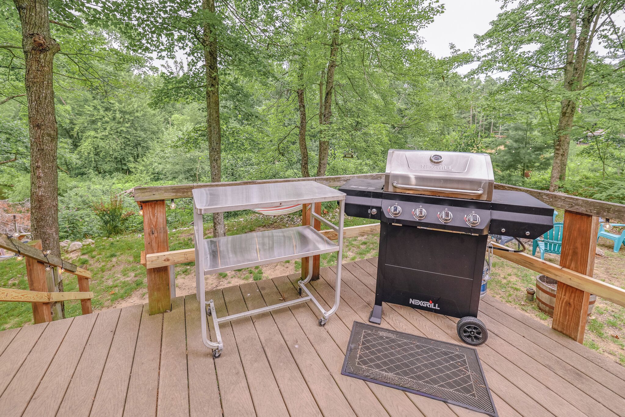 A grill on a deck with a metal cart and a vent.