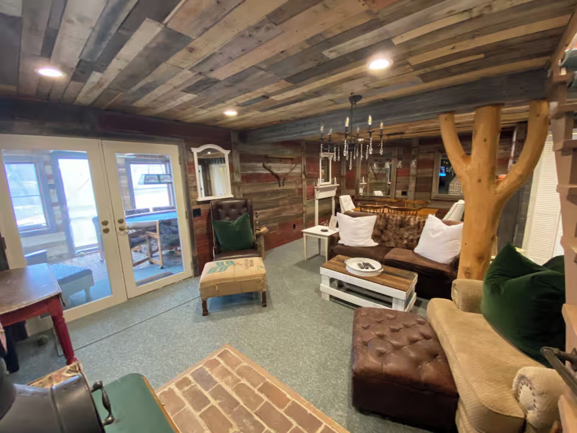 A rustic interior with a wooden ceiling, a sofa set, a dining table, and a large tree trunk.