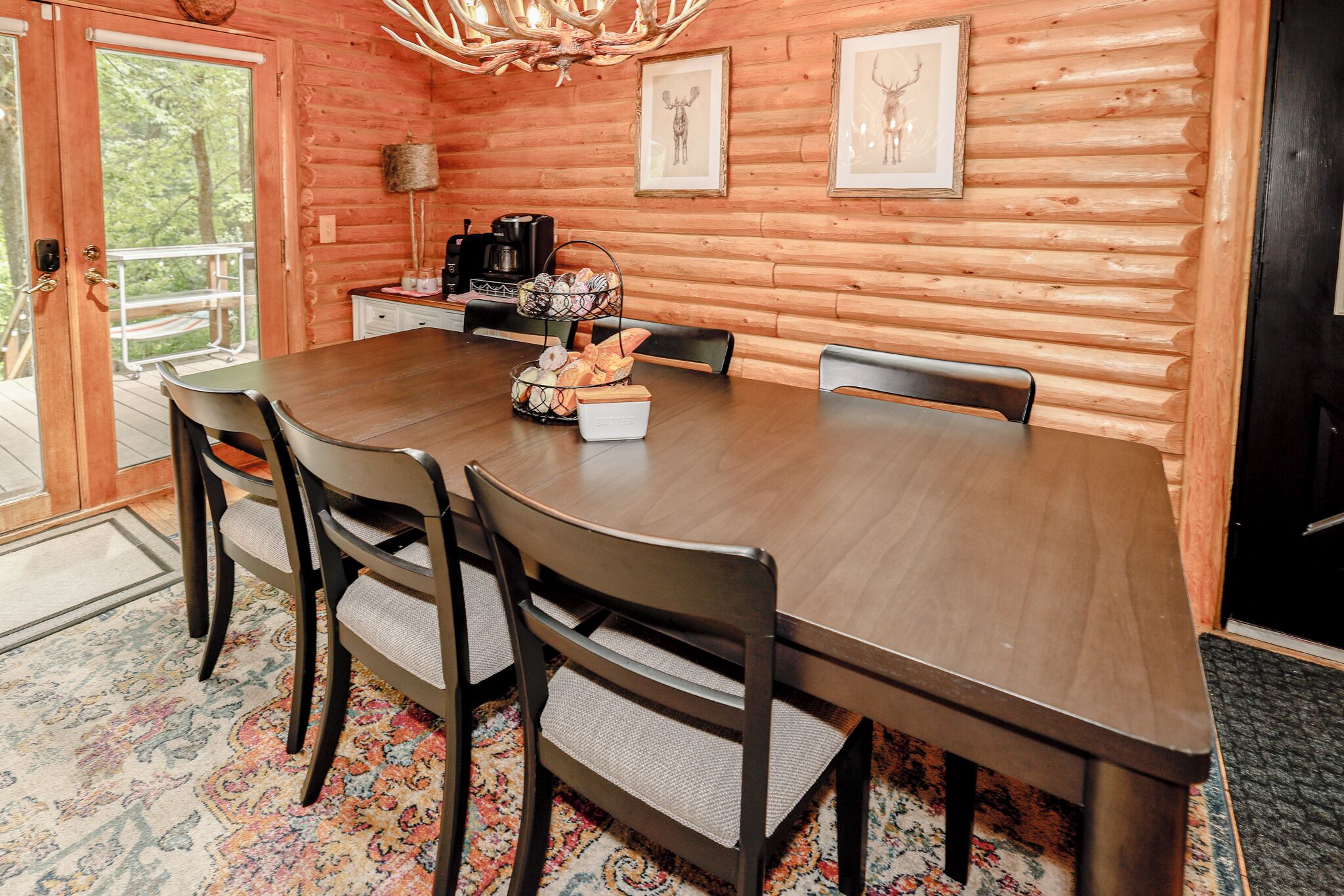 Ein Holzinterieur mit einem Esstisch, Stühlen, einer Kaffeestation und gerahmten Bildern an den Wänden.