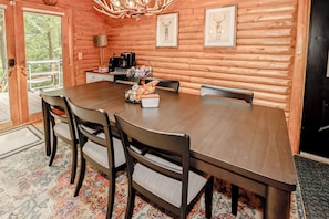 A wooden interior with a dining table, chairs, a coffee station, and framed pictures on the walls.