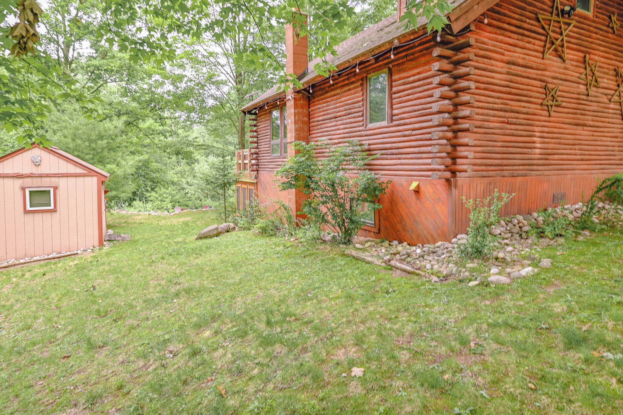 A log cabin with a small shed, surrounded by a grassy yard and trees.