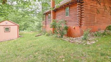 A log cabin with a small shed, surrounded by a grassy yard and trees.