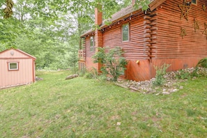 A log cabin with a small shed, surrounded by a grassy yard and trees.