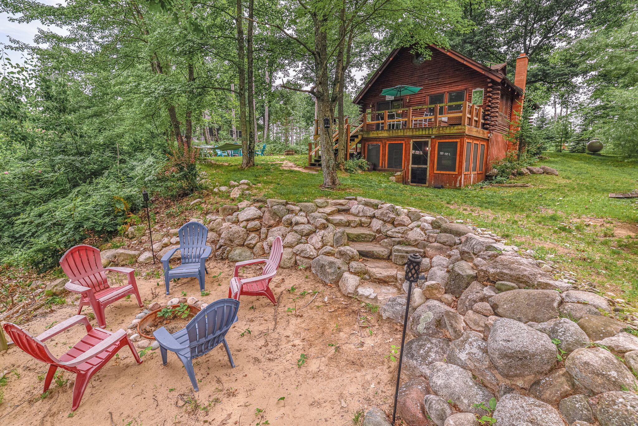 A rustic cabin with a stone fire pit and Adirondack chairs.