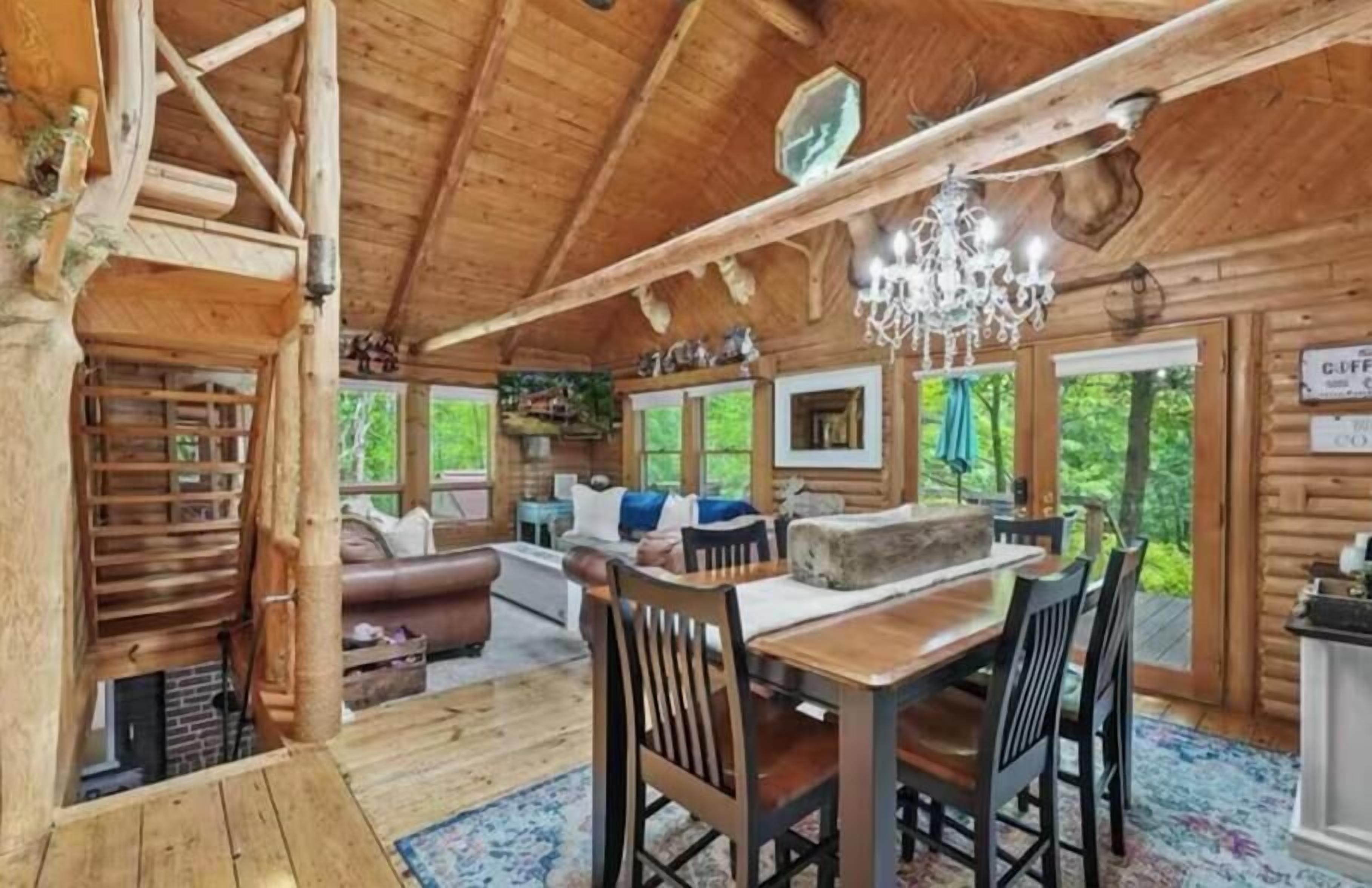 A wooden cabin interior with a dining area, a fireplace, and a chandelier.