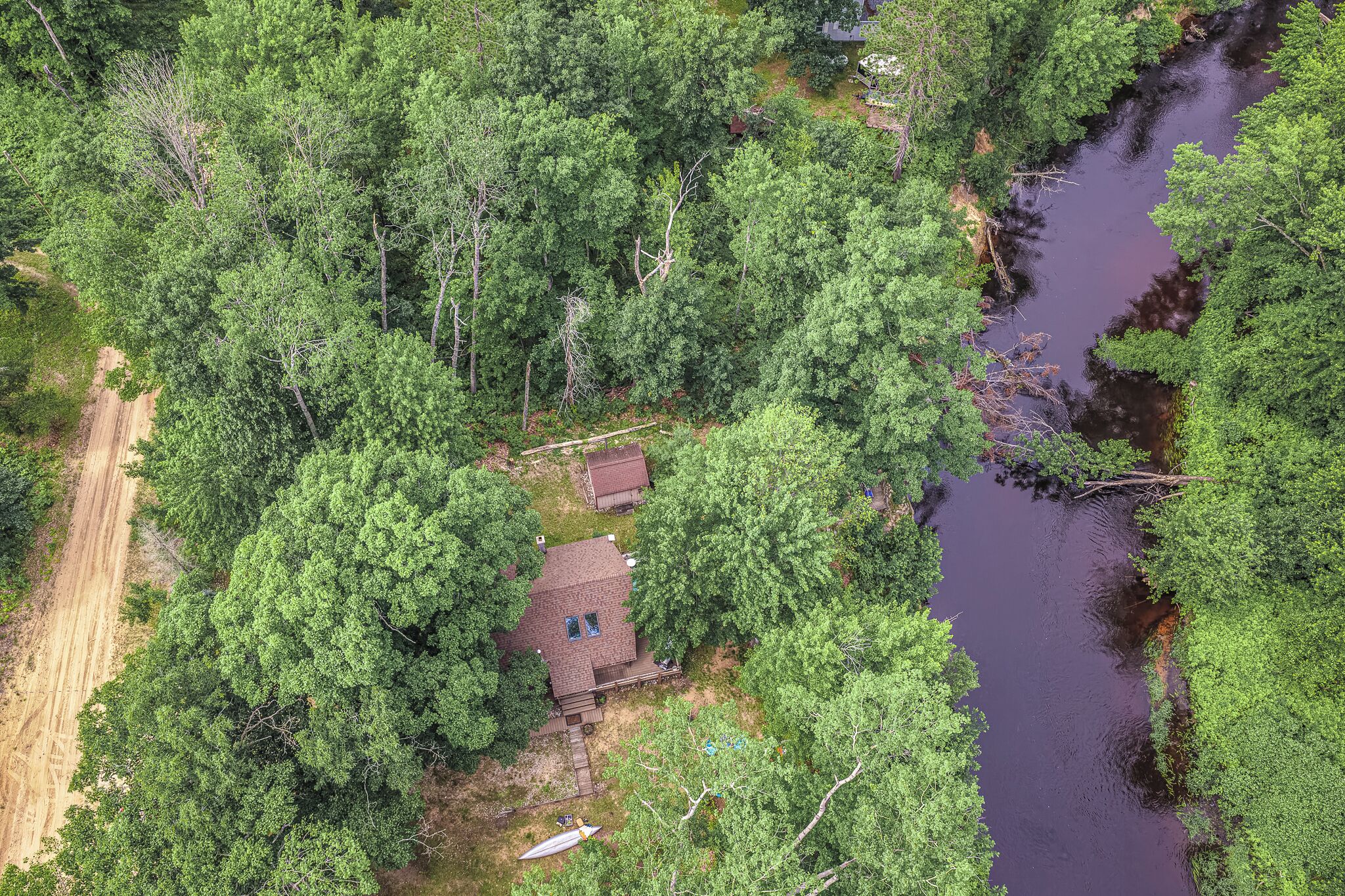 Une vue aérienne d’une zone boisée, avec une maison entourée d’arbres denses et une rivière.
