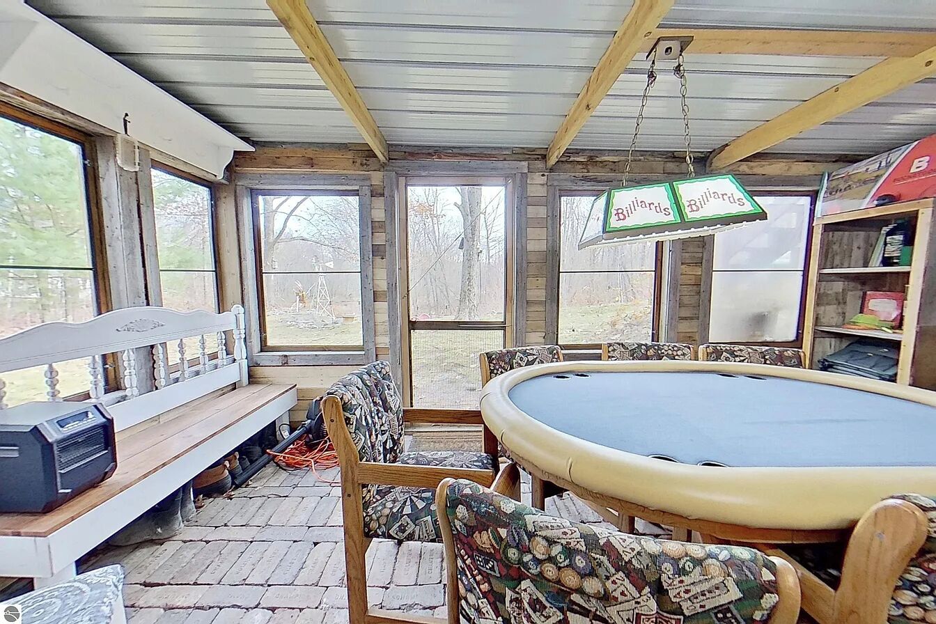 A pool table with chairs, a bench, and a billiards sign in a room with wooden beams and large windows.