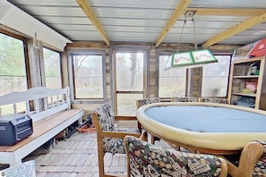 A pool table with chairs, a bench, and a billiards sign in a room with wooden beams and large windows.