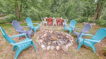 A fire pit surrounded by Adirondack chairs in a forested area.