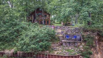 A cabin with a deck and outdoor seating area surrounded by dense forest.