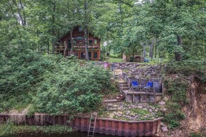 Una cabaña con terraza y zona de estar exterior rodeada de un bosque denso.