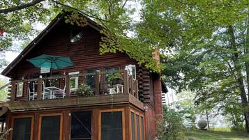 A wooden cabin with a balcony, surrounded by trees and a grassy yard.