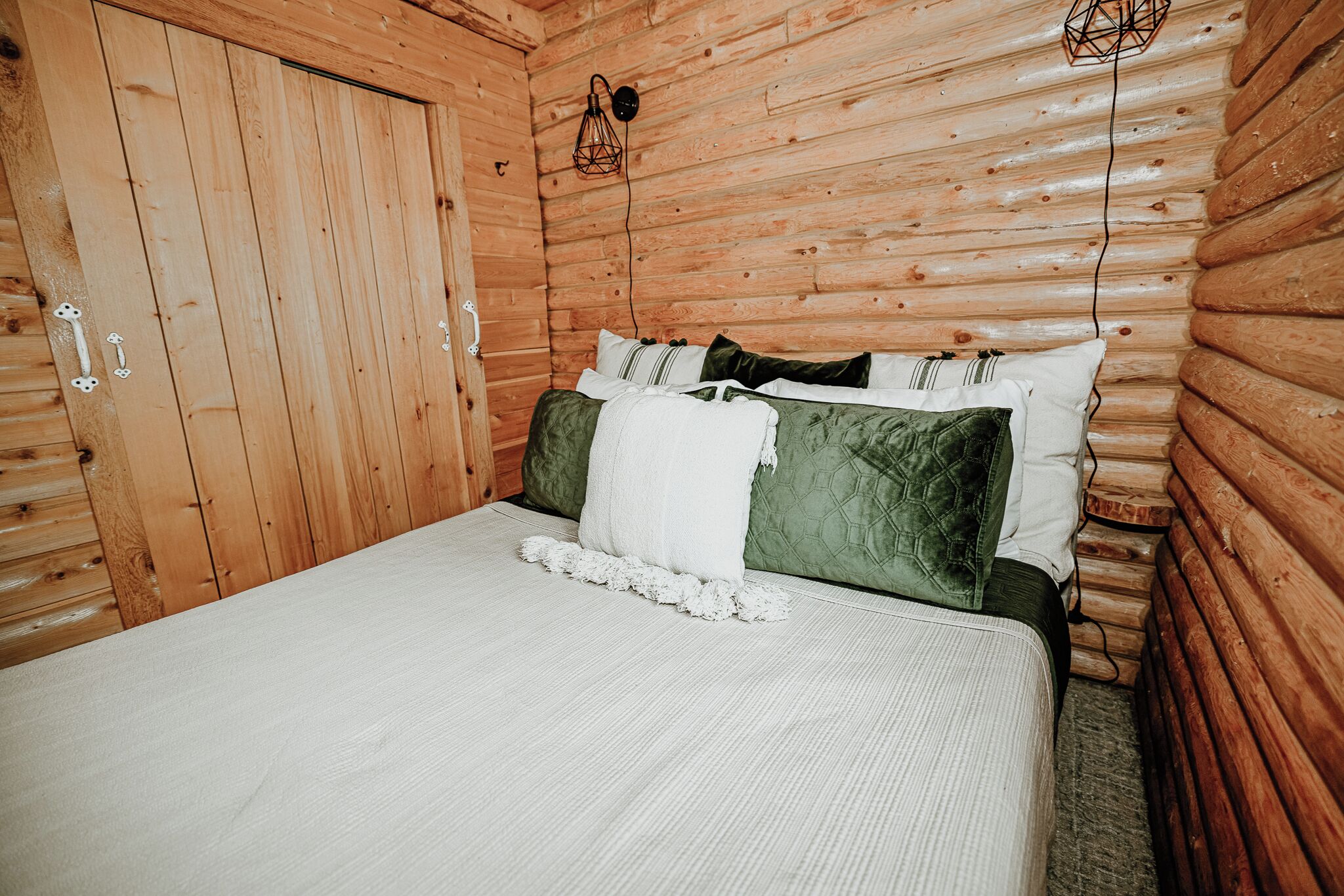 A wooden cabin room with a bed, pillows, and a wall-mounted light fixture.