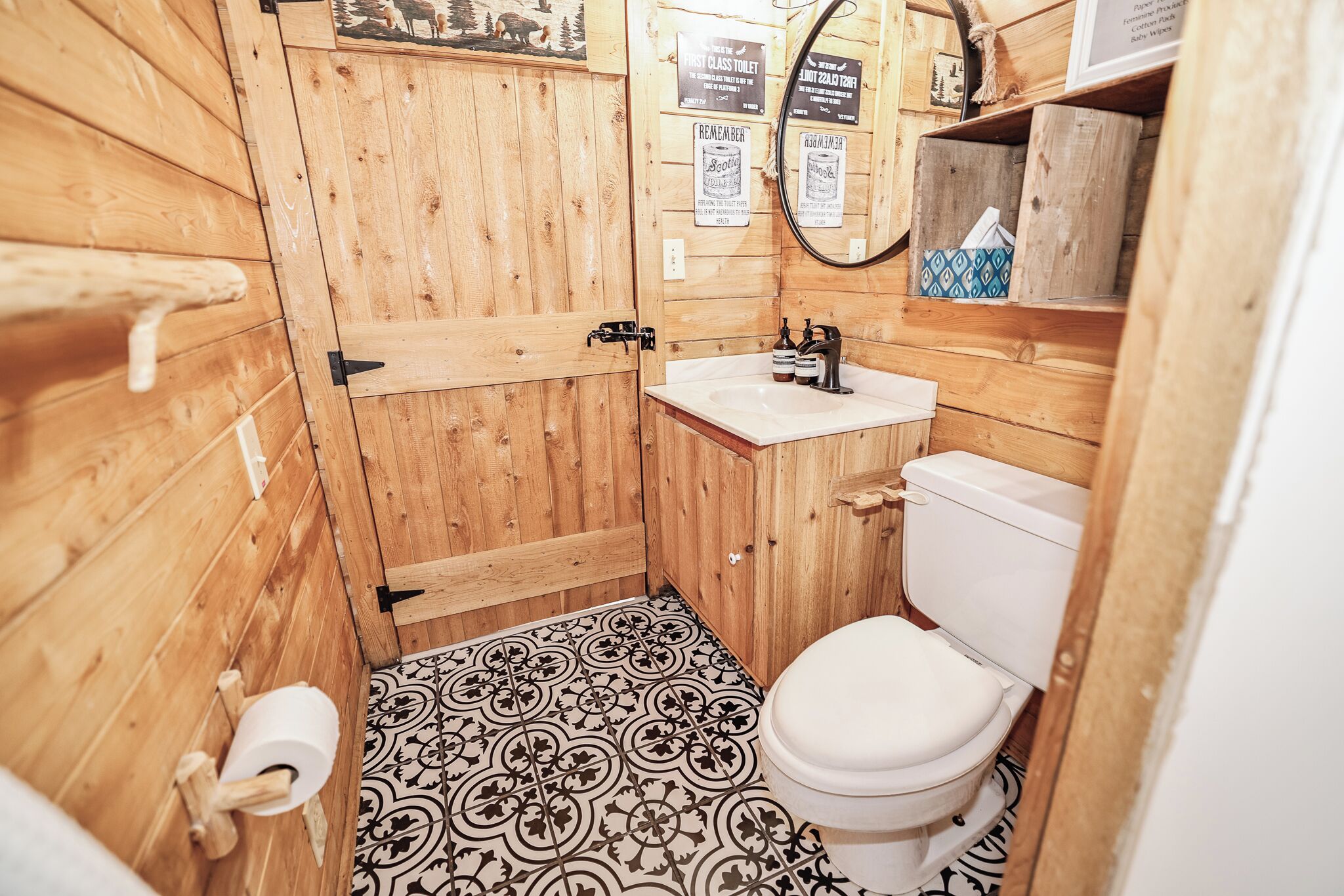 Un baño de madera pequeño y funcional con inodoro, lavamanos y un rollo de papel higiénico.