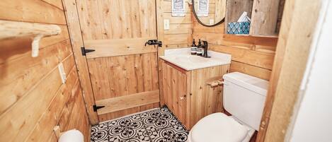 A compact wooden bathroom with a toilet, sink, and a roll of toilet paper.