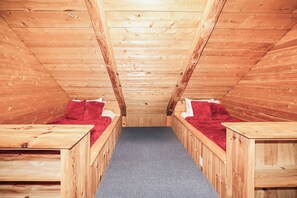 Una habitación con techo inclinado y paredes de madera, con dos camas con ropa de cama roja y alfombra gris.