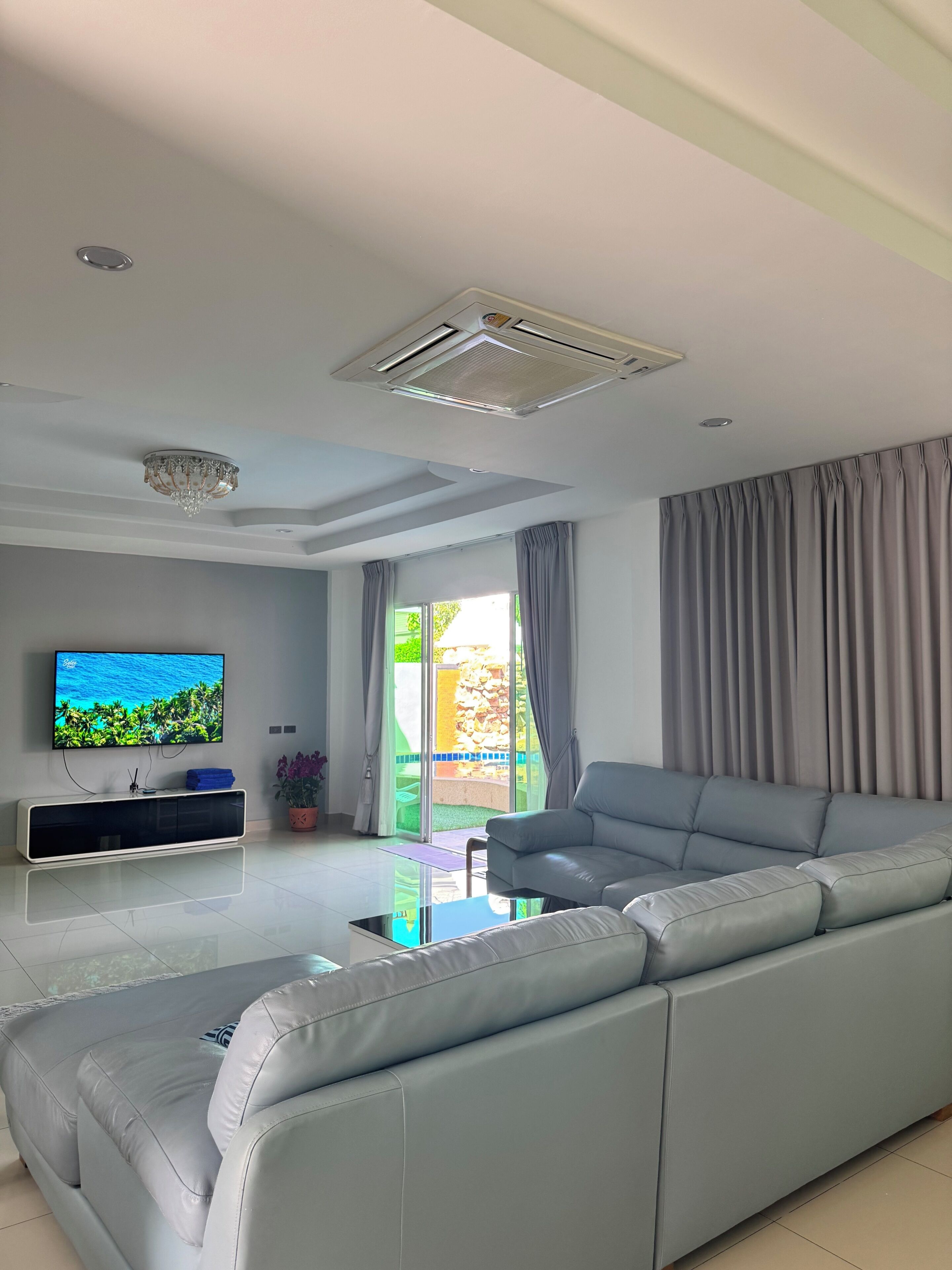 A modern living room with a grey sofa, a flat-screen TV, a ceiling fan, and a sliding glass door leading to an outdoor area.