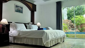 Une chambre d’hôtel avec un grand lit, deux lampes de chevet, un tableau encadré au mur et une vue sur la verdure par la fenêtre.