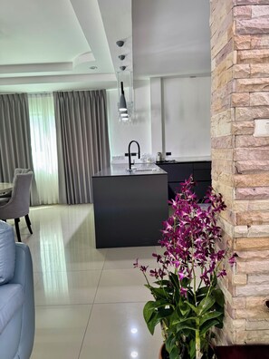 A modern kitchen with a central island, a dining area with a grey sofa, and a potted orchid plant. - Spacious 5-bedroom house in terrific Muang Pattaya with AC and fitness room (Muang Pattaya)