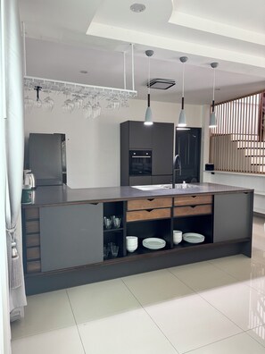 A modern kitchen with a central island, built-in appliances, and pendant lighting. - Spacious 5-bedroom house in terrific Muang Pattaya with AC and fitness room (Muang Pattaya)