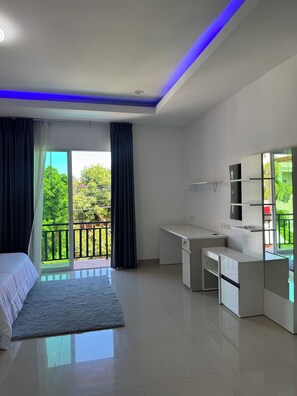 Ein modernes Schlafzimmer mit Bett, Schreibtisch und einem Balkon mit Blick auf Grünflächen.