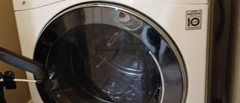 A front-loading LG washing machine with a digital display, a control panel, and a 10-year warranty sticker.