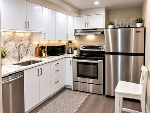 A modern kitchen with stainless steel appliances, white cabinetry, and a marble backsplash.