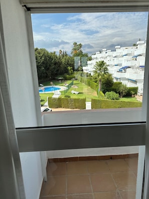 Blick von einem Balkon auf einen Swimmingpool, ordentlich geschnittene Hecken und eine Reihe weißer Gebäude.