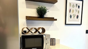 A kitchen with a microwave, a coffee maker, a plant, and a framed tropical leaf art piece.