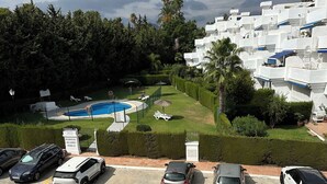 A residential area with a swimming pool, parked cars, and a white building with balconies.