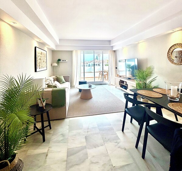 A modern living room with a sofa, coffee table, and dining area with chairs and a TV.