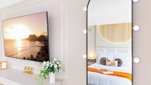 Ein Schlafzimmer mit einem Bett, einem Nachttisch, einem beleuchteten Spiegel, einem an der Wand befestigten Fernseher und einem Fenster mit Sonnenuntergangsblick.