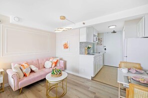 A modern kitchen with white cabinets, a pink sofa, and a dining area with a table and chairs. - @ ML - Bright Waikiki Canal View + Relaxing Breeze (Honolulu)