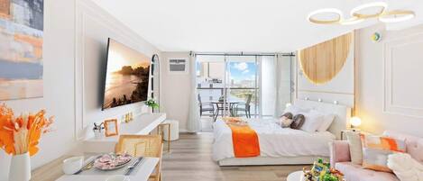 A modern hotel room with a bed, a desk, a dining area, and a view of the city.