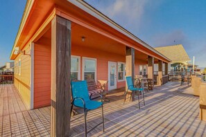 A covered outdoor area with wooden deck, chairs, and tables. - Beach House Steps to Beach (Bolivar Peninsula)