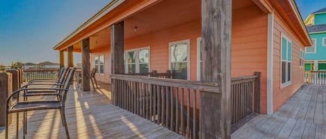 A wooden deck with chairs, a railing, and a building with windows.