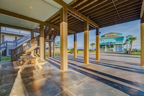 Ein überdachter Außenbereich mit einer Holztreppe, die zu einem Gebäude führt, einem Picknicktisch und Blick auf ein blaues Haus.
