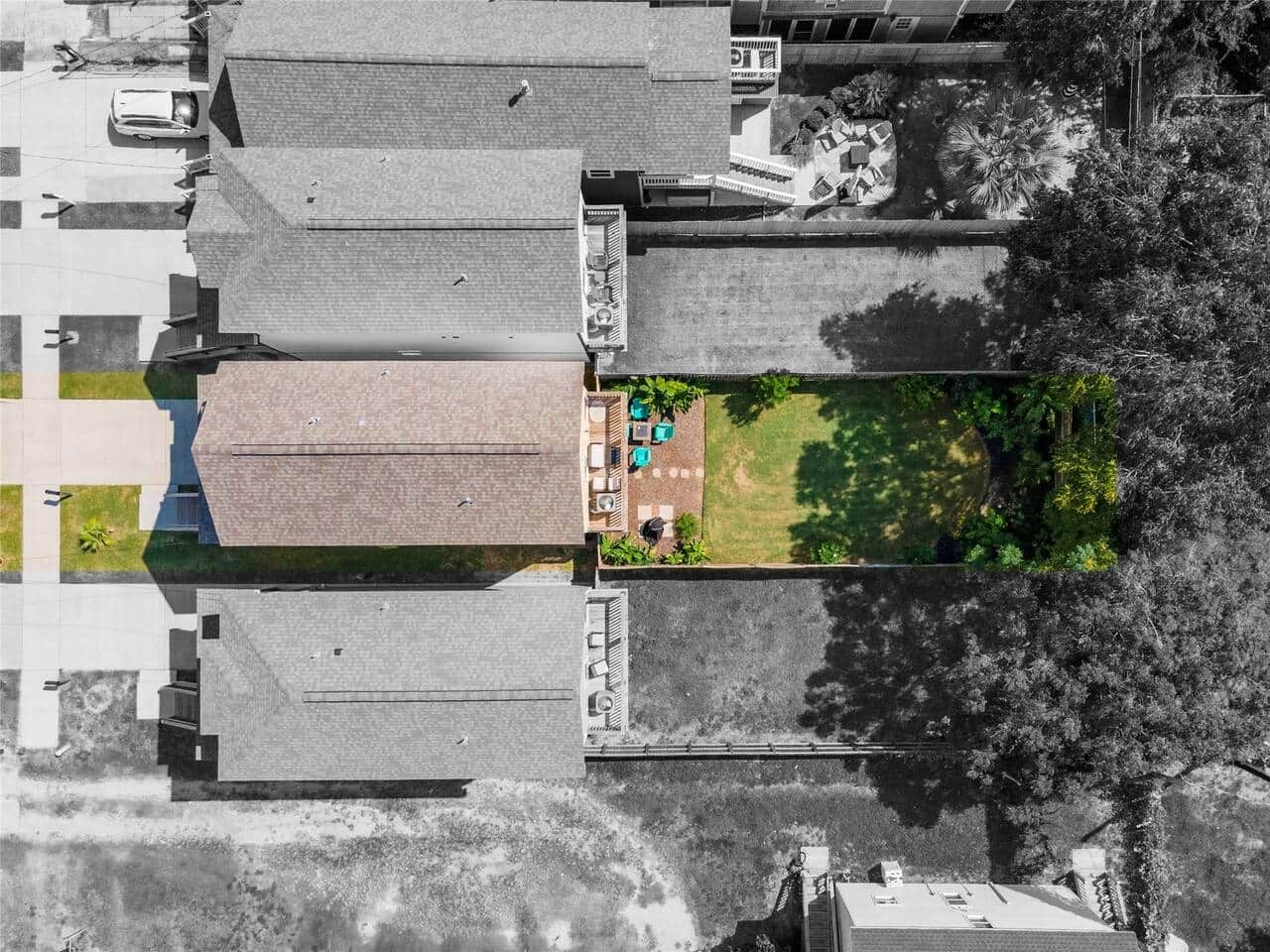 An aerial view of a building with a rooftop terrace, a paved area with outdoor seating, and surrounding trees.