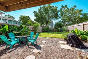 A backyard with a wooden deck, a table with chairs, a grill, and a well-maintained lawn.