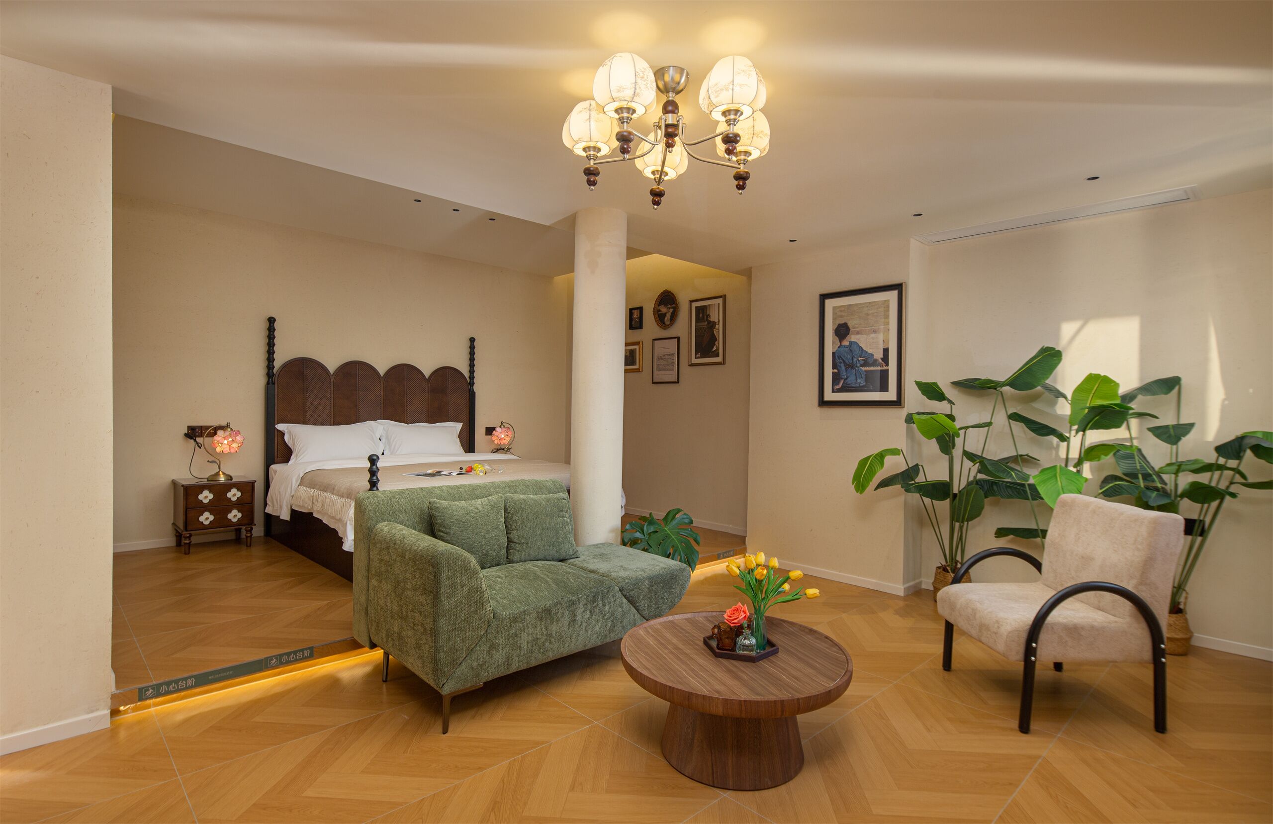 A bedroom with a bed, a green armchair, a wooden coffee table, and a chair with potted plants.