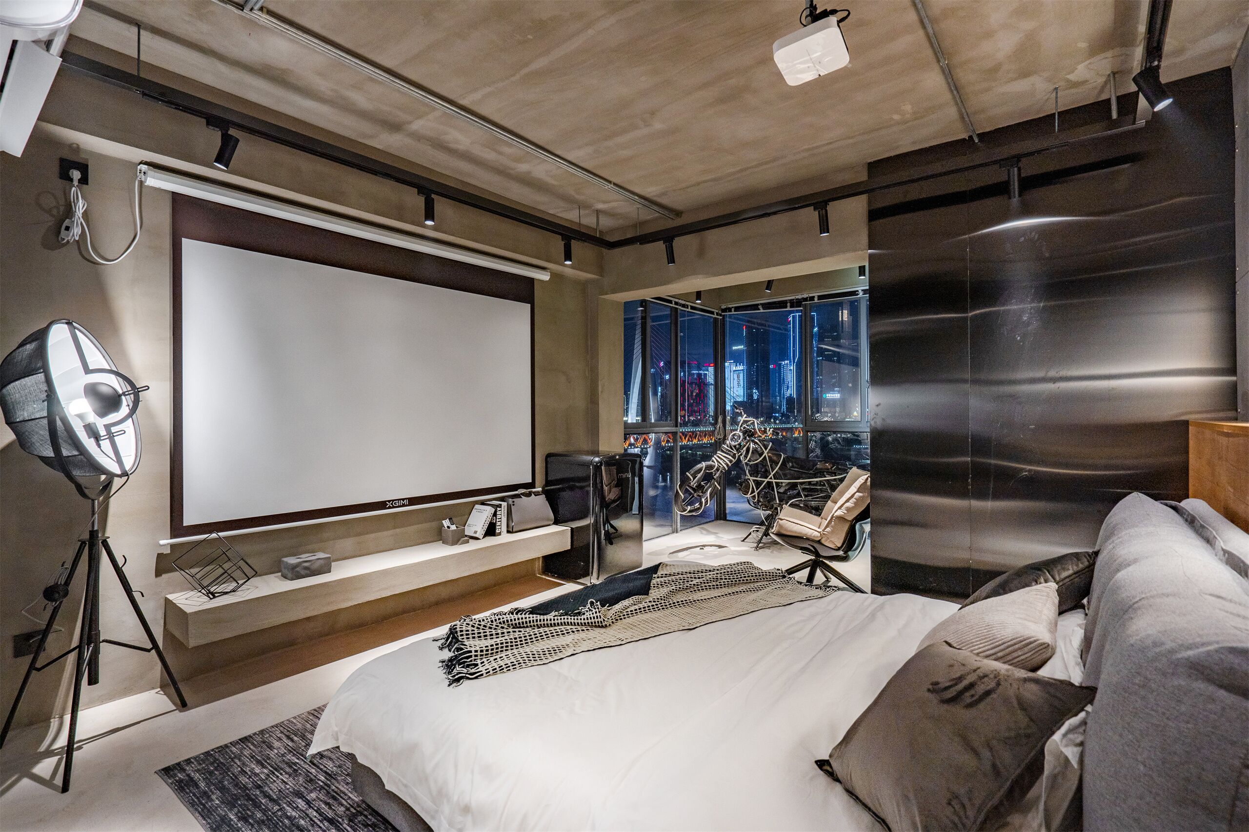 Ein modernes Schlafzimmer mit einem großen Bett, einer Projektionsleinwand und Blick auf die Stadt.