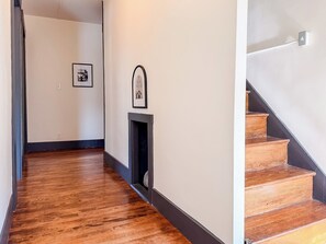 A hallway with wooden flooring, a fireplace, and a staircase. - Downtown - Hot Tub, Speakeasy, Grill, Game Room, Fireplace (Ludlow)