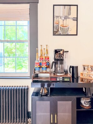 A kitchen area with a coffee machine, Torani syrup bottles, a radiator, and a framed artwork on the wall. - Downtown - Hot Tub, Speakeasy, Grill, Game Room, Fireplace (Ludlow)