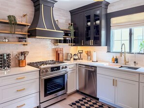 A modern kitchen with stainless steel appliances, black cabinetry, and a checkered floor mat. - Downtown - Hot Tub, Speakeasy, Grill, Game Room, Fireplace (Ludlow)